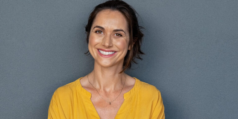 Happy mature woman smiling on grey wall