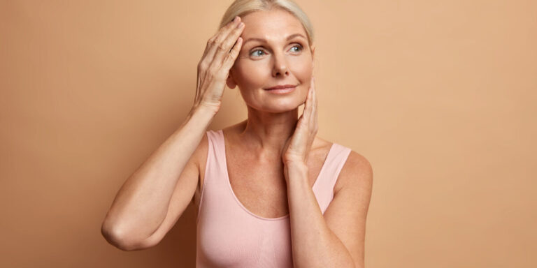 Portrait of mature elderly European woman touches face gently has perfect skin and looks thoughtfully away enjoys her soft complexion cares about appearance satisfied after anti aging procedure