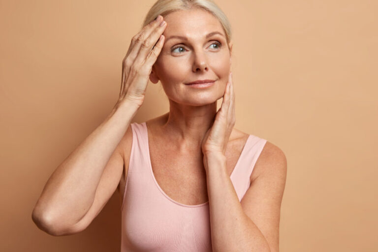 Portrait of mature elderly European woman touches face gently has perfect skin and looks thoughtfully away enjoys her soft complexion cares about appearance satisfied after anti aging procedure