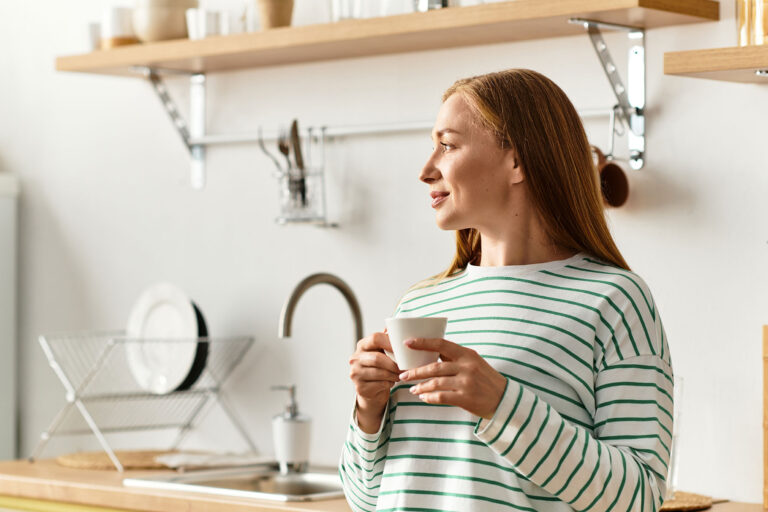 Ästhetische Behandlungen - Schönheitschirugie Bönen - Frau mit Kaffee steht in der Küche und schaut zum Fenster raus