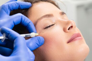 Attractive young woman is getting a rejuvenating facial injections. She is sitting calmly at clinic. The expert beautician is filling female wrinkles by hyaluronic acid.