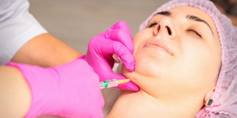 The cosmetologist makes lipolytic injection on the chin of a young woman against the double chin in a beauty salon.