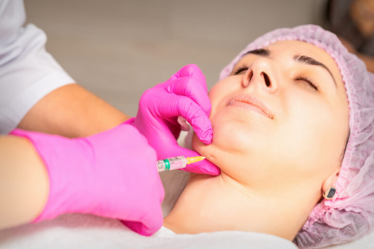 The cosmetologist makes lipolytic injection on the chin of a young woman against the double chin in a beauty salon.
